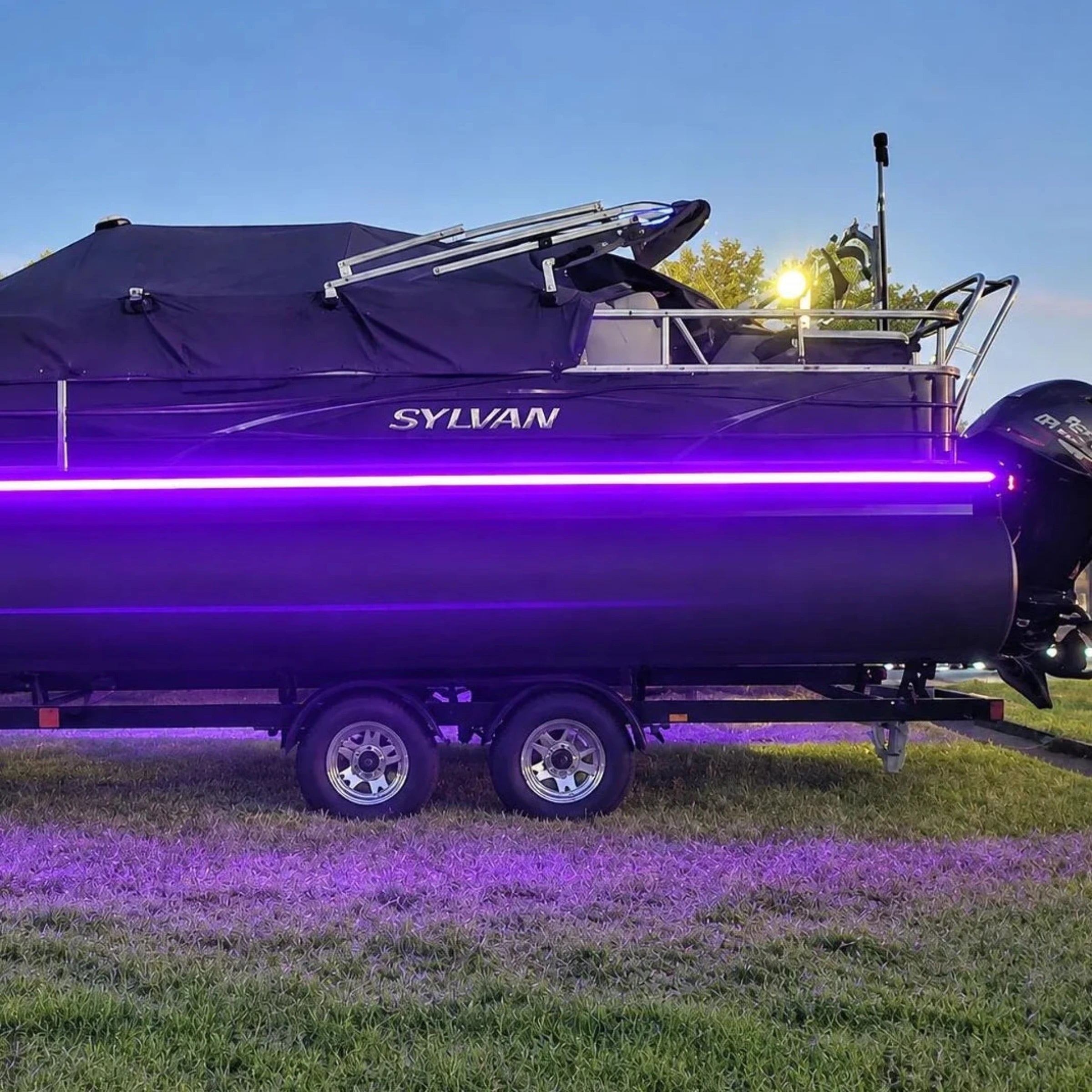 Purple boat with LED lights on a trailer, branded 'Sylvan', against a clear blue sky.