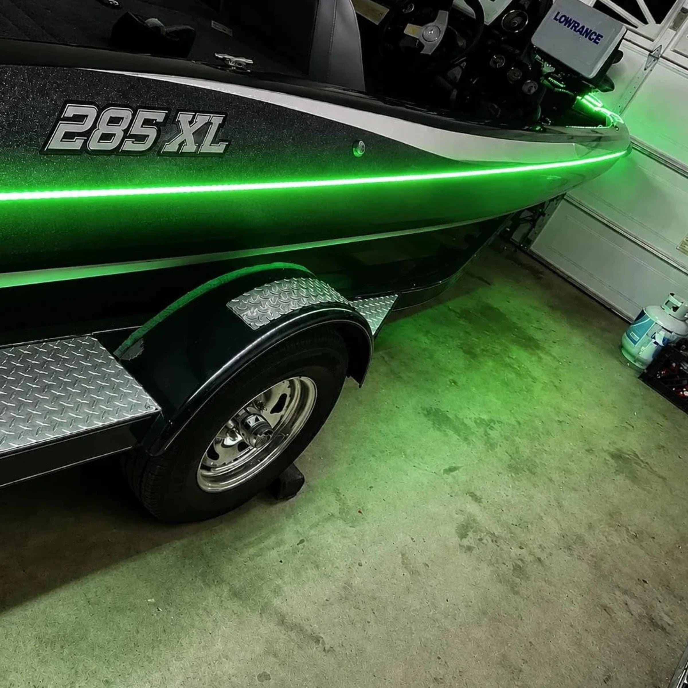 Green boat with '285 XL' on a trailer in a garage.